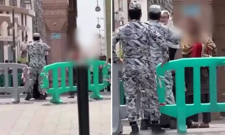 Two security officers confront a woman near a barricade outside the Prophet’s Mosque in Madinah, with the mosque and city structures in the background. The image is blurred for privacy.