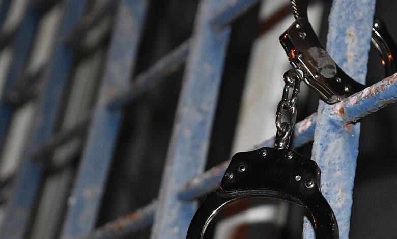 Handcuffs hang on a prison cell gate symbolizing arrest