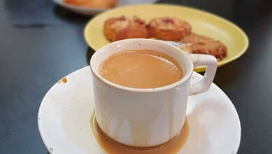 A cup of irani chai with biscuits in the background