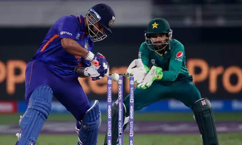 A couple of men playing cricket outdoors on a grassy field, wearing sports uniforms and using cricket bats and balls in a game setting.
