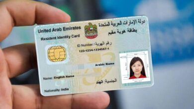 Representative image shows a person holding a UAE Emirates ID card for a resident, featuring a smart chip, ID number, and a passport-sized photo of a woman. The ID displays English and Arabic text, including the name field and nationality marked as India. The background is blurred, highlighting the identification card in focus.