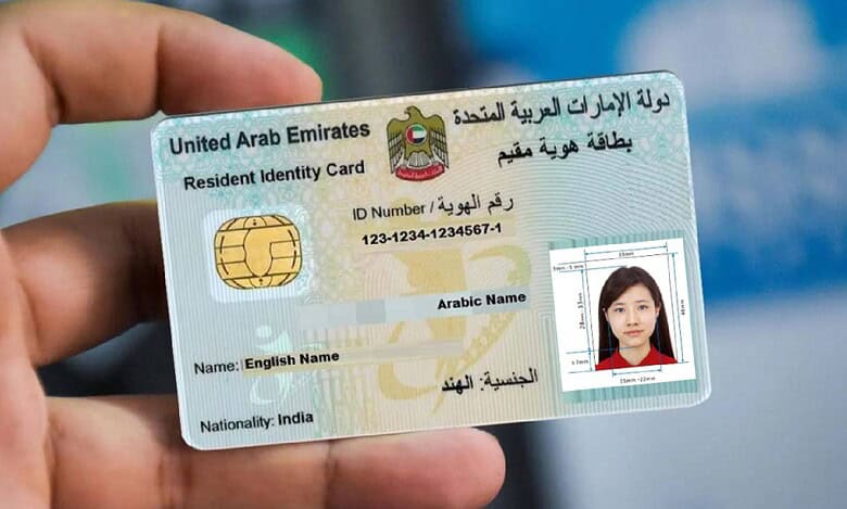 Representative image shows a person holding a UAE Emirates ID card for a resident, featuring a smart chip, ID number, and a passport-sized photo of a woman. The ID displays English and Arabic text, including the name field and nationality marked as India. The background is blurred, highlighting the identification card in focus.