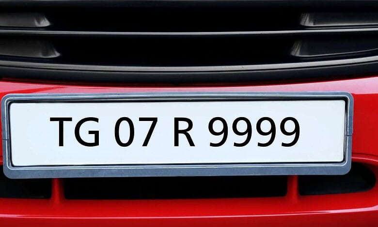 A red car's front bumper with a white license plate, gray border, showing "TG 07 R 9999" in black. "TG" is Telangana, "07" is RTO code, "R 9999" is the vehicle number. Black air vents are above and below the plate.