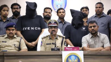 A group of people, including police officers and four arrested individuals, two with their faces covered, are at a press conference