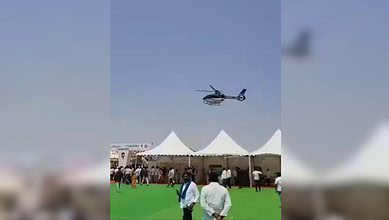 A helicopter hovers low over tents at the Rythu Mahotsav event in Nizamabad, as people look on and begin to move away.