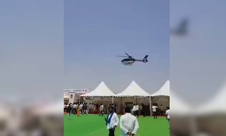 A helicopter hovers low over tents at the Rythu Mahotsav event in Nizamabad, as people look on and begin to move away.