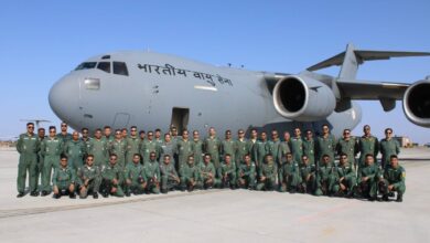 A group of uniformed personnel poses in front of a large Indian Air Force transport aircraft on the tarmac under a clear sky.