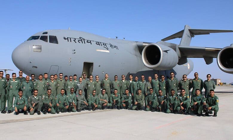 A group of uniformed personnel poses in front of a large Indian Air Force transport aircraft on the tarmac under a clear sky.