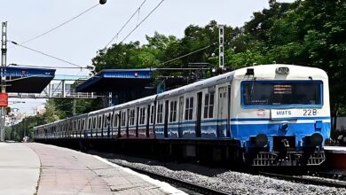 MMTS train parked at a Hyderabad platform with blue and white livery, under a canopy with green trees behind.