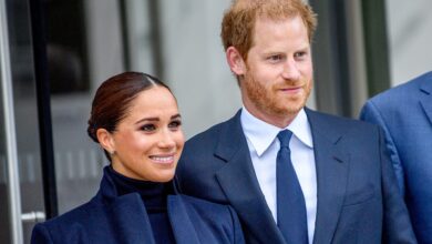 Photo of Prince Harry and Meghan Markle wearing formal navy outfits, smiling and standing together outside a building.