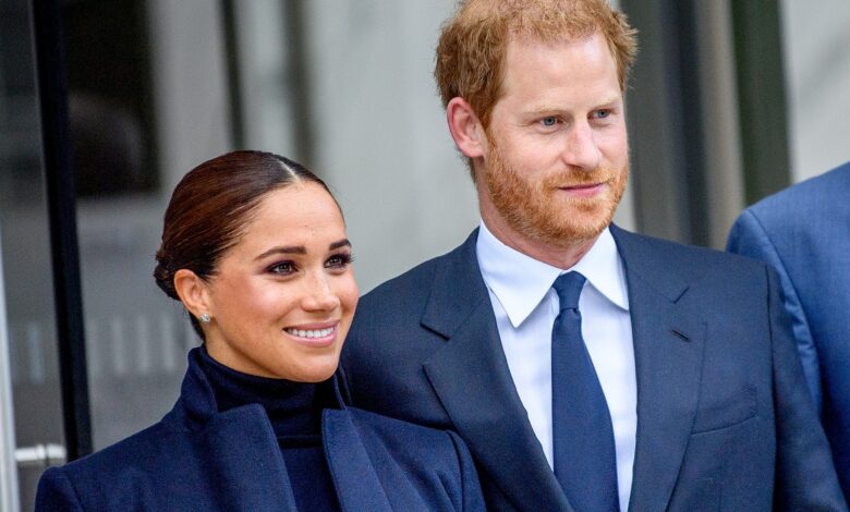 Photo of Prince Harry and Meghan Markle wearing formal navy outfits, smiling and standing together outside a building.