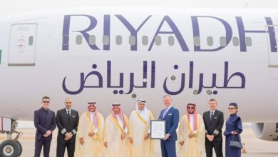 A group of dignitaries, executives, and crew members pose in front of a Riyadh Air airplane.