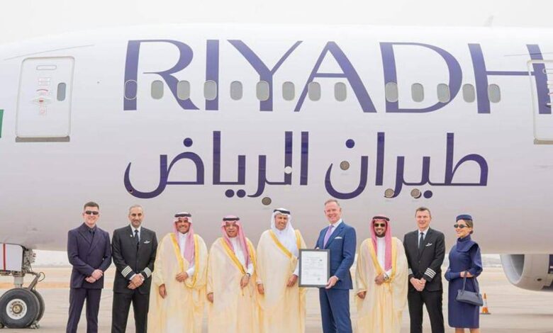 A group of dignitaries, executives, and crew members pose in front of a Riyadh Air airplane.