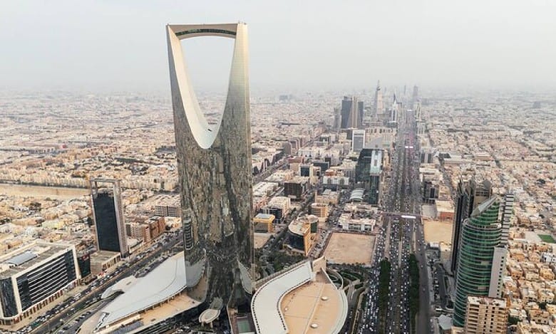 Aerial view of Riyadh city skyline, Saudi Arabia, featuring the iconic Kingdom Centre Tower and surrounding modern skyscrapers on a hazy day.