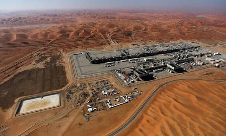 Aerial view of oil or gas processing facility in the Saudi Arabian desert, surrounded by sand dunes under clear skies.