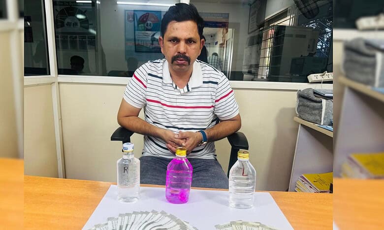 A man in a striped shirt sits at a desk with Rs 2,22,000 in cash, two water bottles labeled "L" and "R," and a pink liquid bottle, linked to a bribery arrest by Shamirpet police.