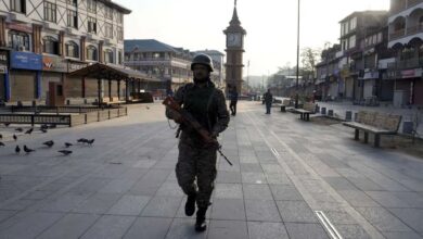 The image displays a picture of a security personnel standing guard at Lal Chowk market