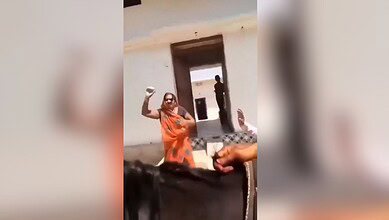 The image shows a woman in an orange saree throwing stones