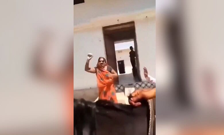 The image shows a woman in an orange saree throwing stones