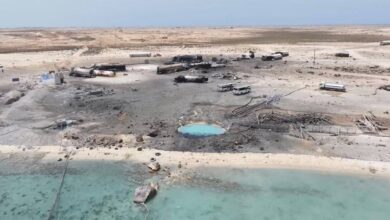 Aerial view of charred vehicles and damaged fuel tankers at Ras Isa fuel port in Al Jazirah, Yemen, reportedly after a US airstrike, with debris scattered across the desert landscape near the shoreline.