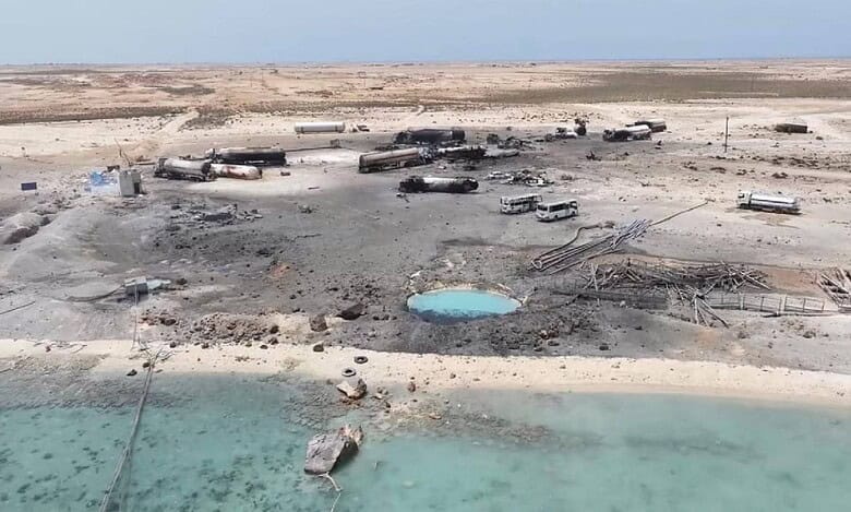 Aerial view of charred vehicles and damaged fuel tankers at Ras Isa fuel port in Al Jazirah, Yemen, reportedly after a US airstrike, with debris scattered across the desert landscape near the shoreline.