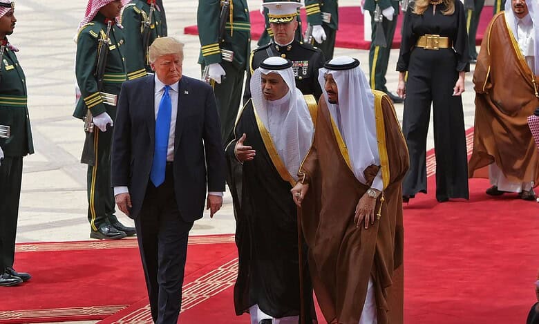 Donald Trump walks alongside Saudi King Salman on a red carpet at King Khalid International Airport, flanked by officials and ceremonial guards, with Melania Trump following behind.