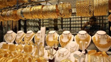 Display of traditional gold jewellery including necklaces, bangles, and earrings in a shop at Dubai Gold Souk, with a shopkeeper seen in the background.