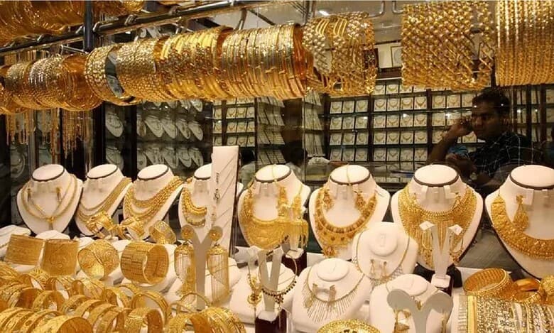 Display of traditional gold jewellery including necklaces, bangles, and earrings in a shop at Dubai Gold Souk, with a shopkeeper seen in the background.