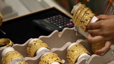 A person arranges gold bangles in a jewellery store with a calculator in the background, highlighting gold retail business activity.
