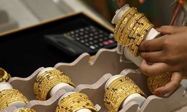 A person arranges gold bangles in a jewellery store with a calculator in the background, highlighting gold retail business activity.