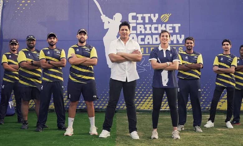 Smriti Mandhana with coach Don Bhagawati and the coaching team at the launch of City Cricket Academy by Smriti Mandhana in Dubai, standing in front of the academy banner on a cricket ground.