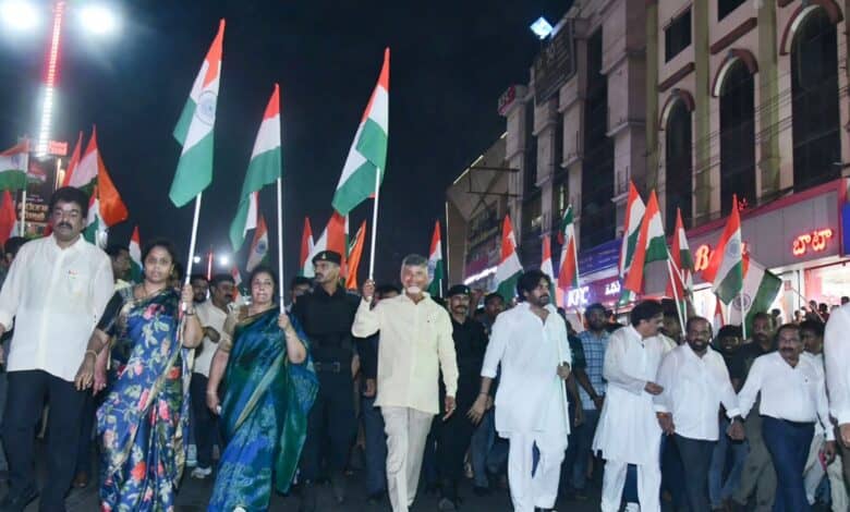A large group marches at night holding Indian flags, including leaders and civilians, celebrating national unity and pride.