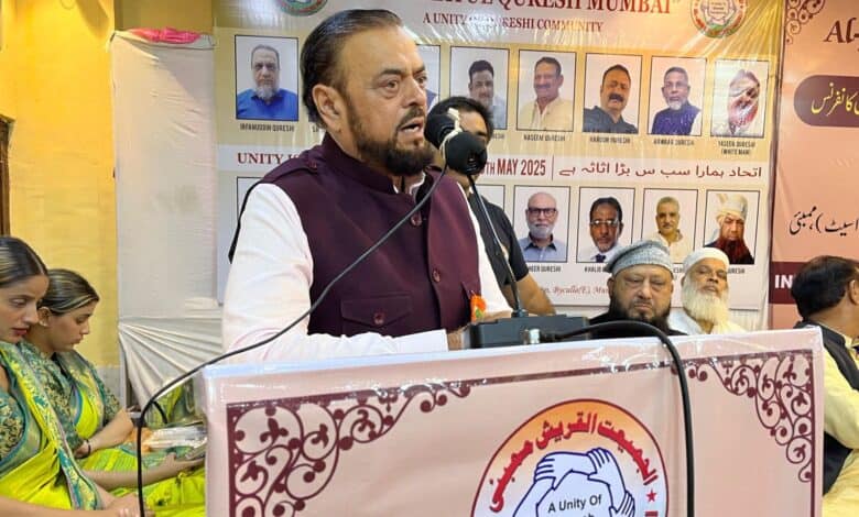 Man speaks at Al-Jamiatul Quresh Mumbai event, surrounded by guests and banners promoting unity in the Qureshi community.