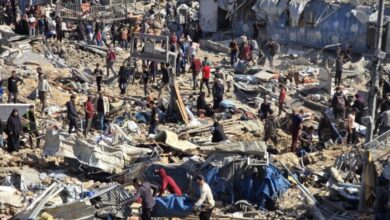 A chaotic scene of destruction in Gaza, with dozens of Palestinians standing amidst rubble and debris from recent Israeli airstrikes. Collapsed buildings, scattered belongings, and makeshift shelters are visible, as people appear to search for survivors or belongings.