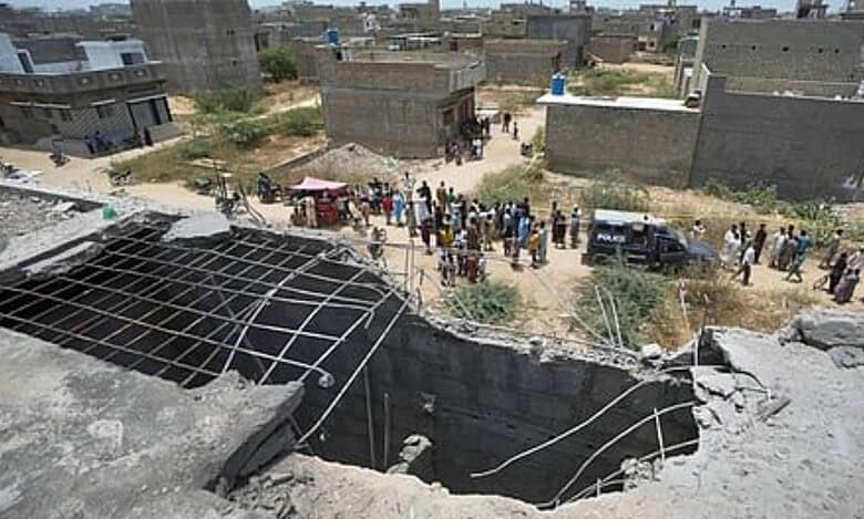 A large hole is visible on the rooftop of a structure reportedly damaged in a suspected Indian drone strike, as residents gather near a cordoned-off area where Pakistan's air defence system shot down the drone in Karachi on May 8.