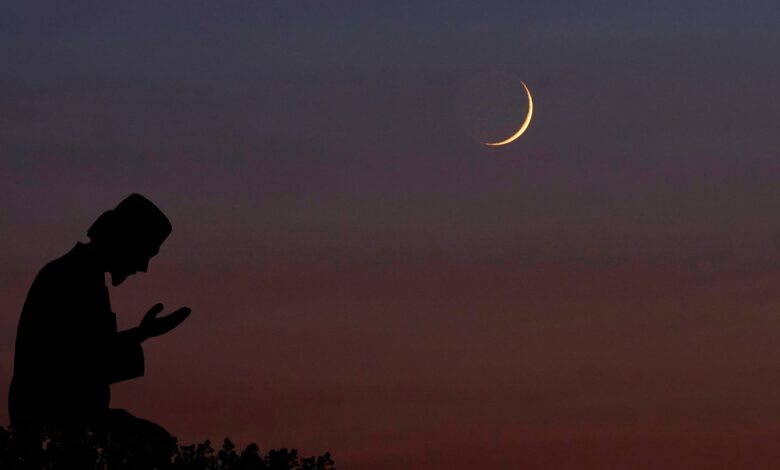 A silhouette of a person praying under a twilight sky with a crescent moon visible above.