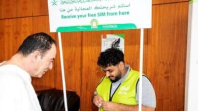 A Haj pilgrim receives assistance from a staff member at a counter distributing free SIM cards in Saudi Arabia.