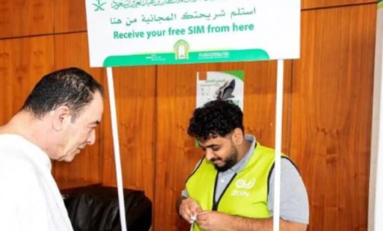 A Haj pilgrim receives assistance from a staff member at a counter distributing free SIM cards in Saudi Arabia.