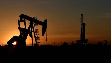Silhouette of an oil pumpjack and drilling rig at sunset in an oil field.