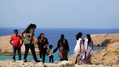 Group of people enjoying a scenic view of the Indian Ocean from a rocky hilltop in Bandar Al Khairan, Oman, with turquoise waters and rugged cliffs in the background.