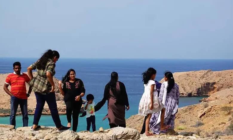 Group of people enjoying a scenic view of the Indian Ocean from a rocky hilltop in Bandar Al Khairan, Oman, with turquoise waters and rugged cliffs in the background.