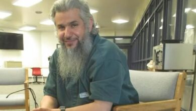 Saudi citizen Homaidan Al-Turki sitting in a detention facility, smiling slightly while holding eyeglasses.