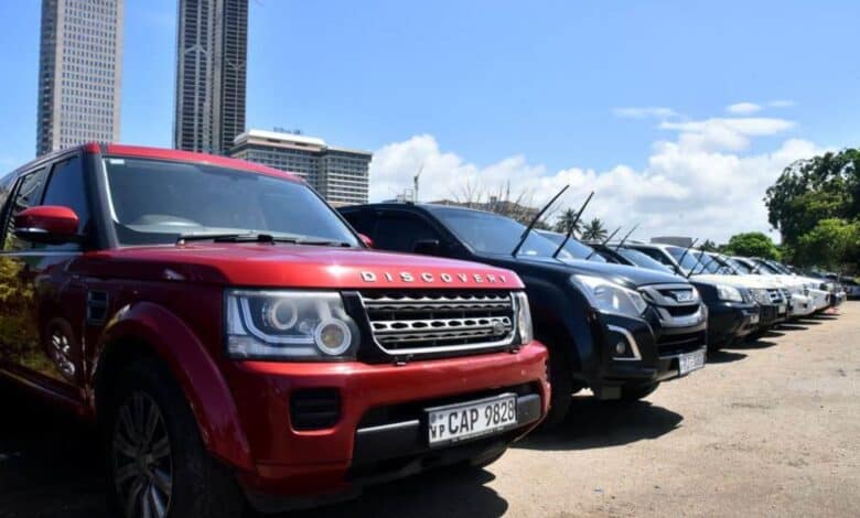 Row of parked SUVs including a red Land Rover Discovery, with tall city buildings and a clear blue sky in the background.