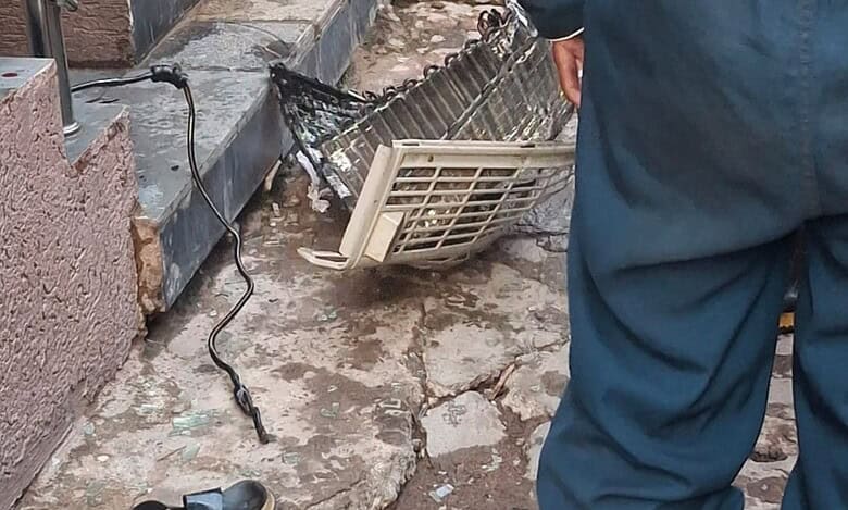 AC parts scattered on the floor with firefighters standing nearby responding to the aftermath of an AC blast in Talab Katta that injured two individuals