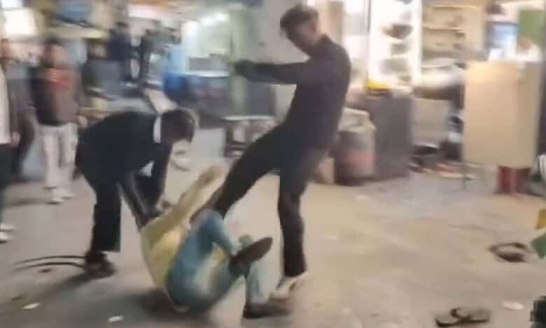 The image displays a picture of two men kicking a man in yellow shirt in Nanital