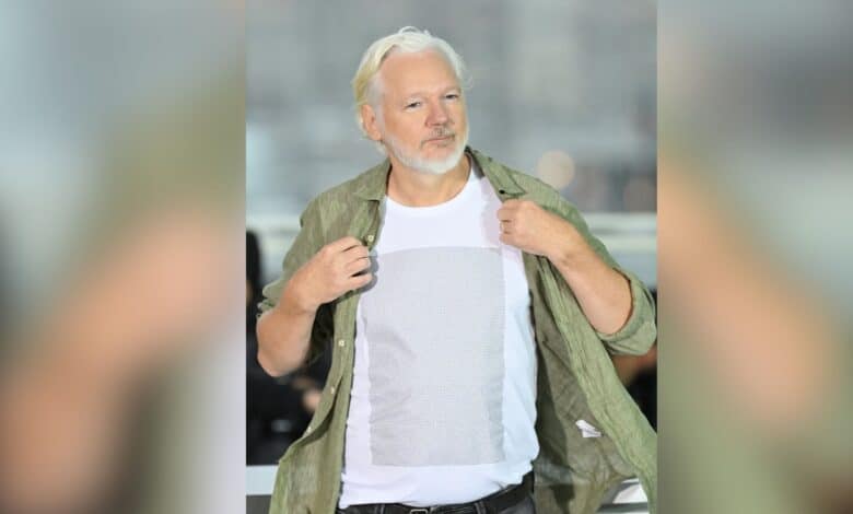 The image displays a picture of WikiLeaks founder Julian Assange at the 78th Cannes Film Festival in France wearing a T-shirt with the names of Palestinian children killed by Israeli forces since 2023.