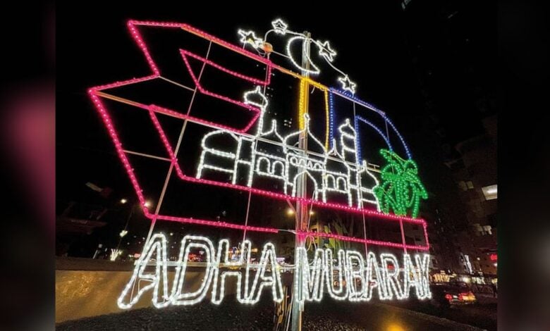 Eid Al Adha light decoration with mosque, crescent moon, and Adha Mubarak message in vibrant colours at night.