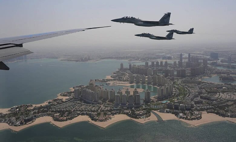 Qatar Emiri Air Force F-15 fighter jets escort Air Force One over The Pearl in Doha, Qatar, with the city's coastal skyline visible below on a clear day.