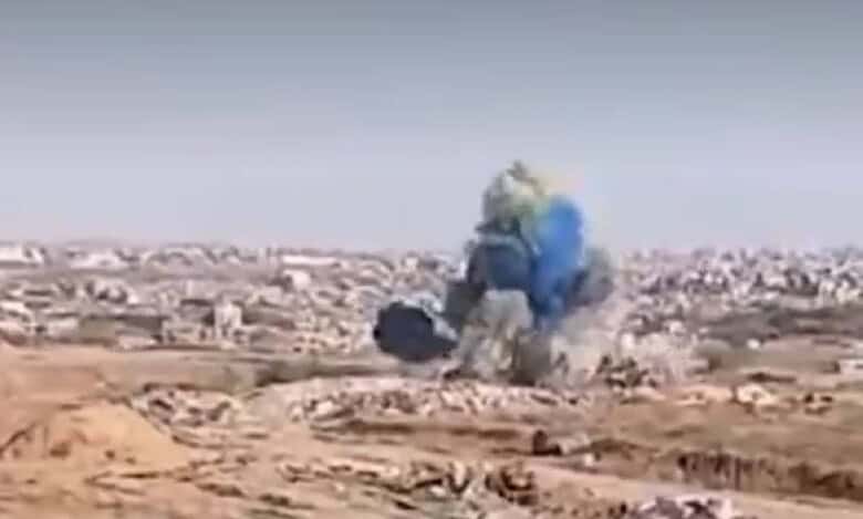 Explosion in Gaza releasing blue smoke, allegedly part of a gender reveal by Israeli soldiers, with urban ruins visible in the background.