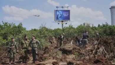 Israeli security forces inspect impact site of Houthi missile near Ben Gurion Airport, with visible damage and airport control tower in the background.